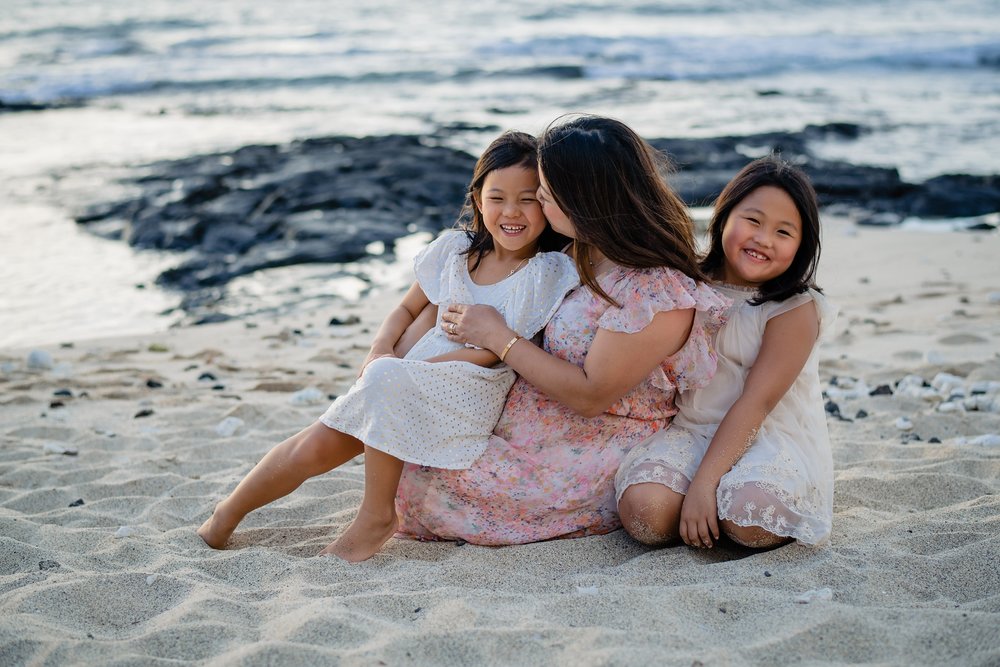happy mom and daughters sitting on Hawaii white sand