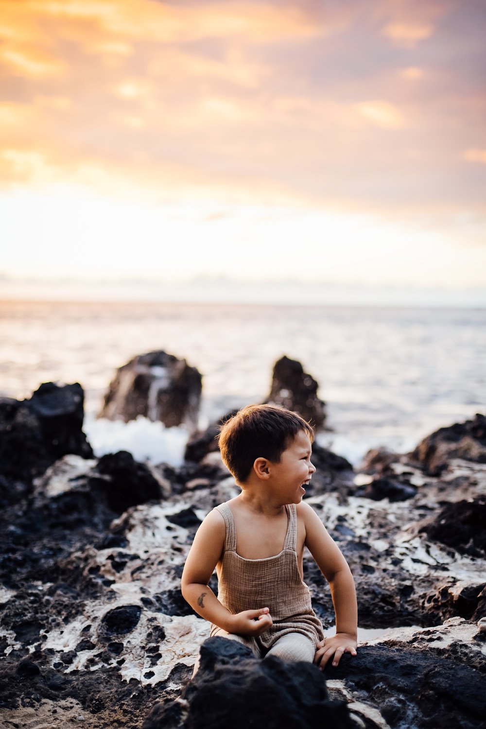 Boy playing on lava rocks during family session in hawaii