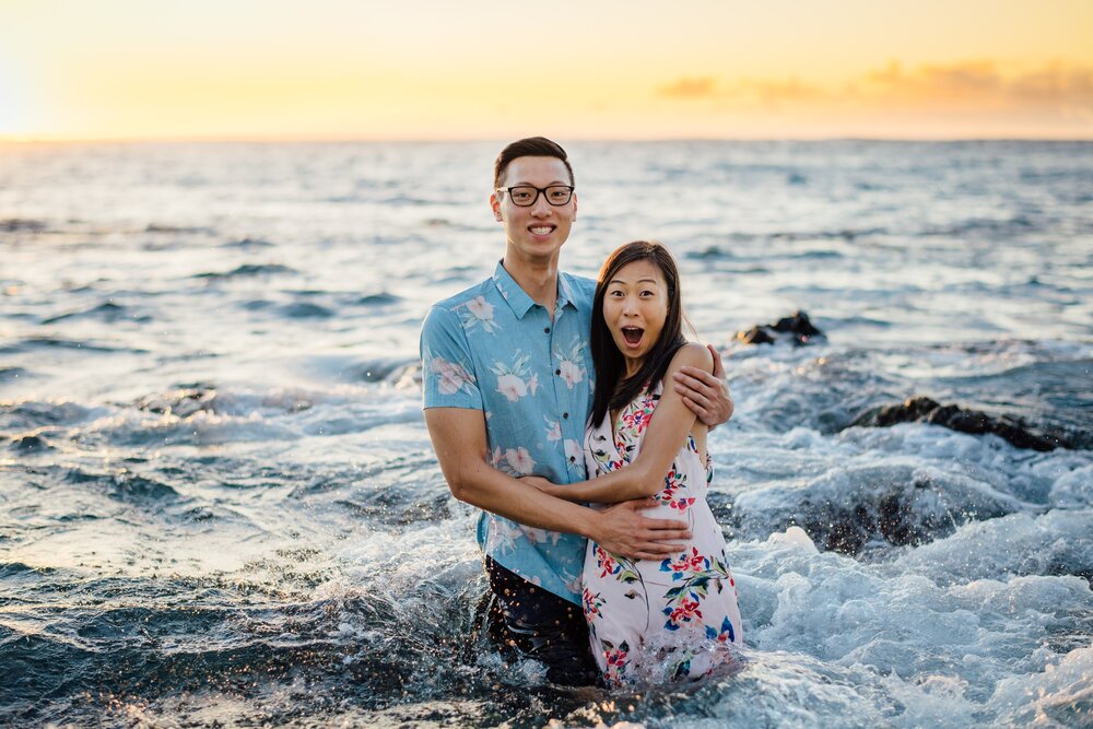 A wave hits a couple during their engagement session in Kona
