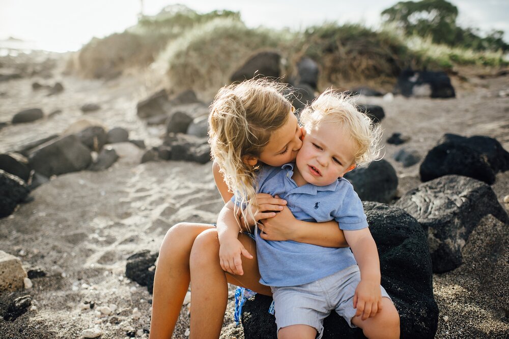 big sister kissing little brother on the lava rocks