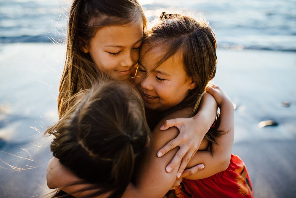 sisters embracing on a beach in hawaii during family photo session