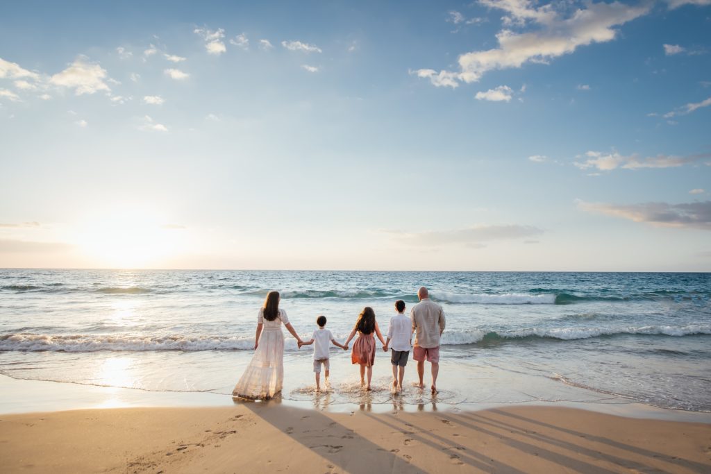 family holding hands at the beach by holiday family photographer