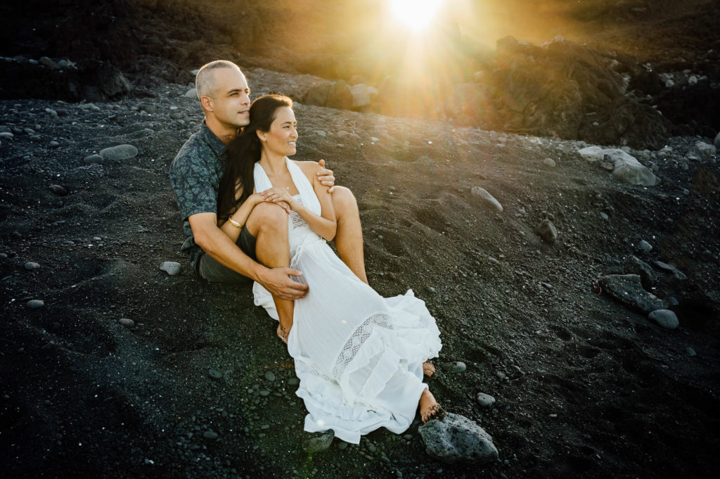 couple sitting on black sand during the sunset