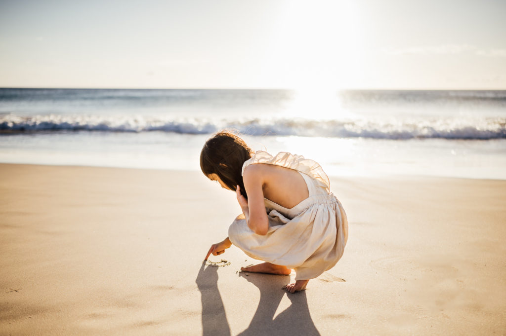 young girl writing on the white sand by vacation photographer