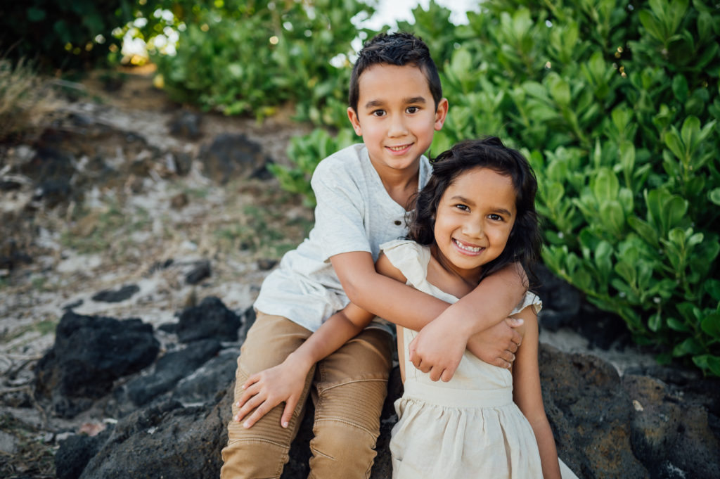 cute siblings smiling and sitting on lava rocks