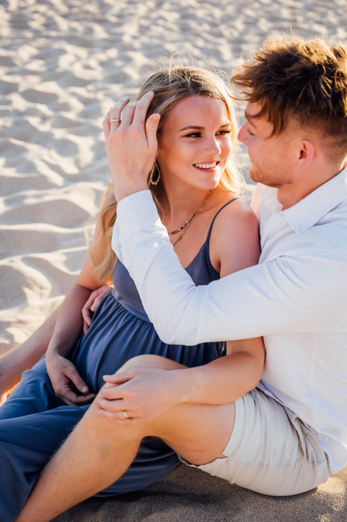 couple sitting on the sand while husband stroking wife's hair