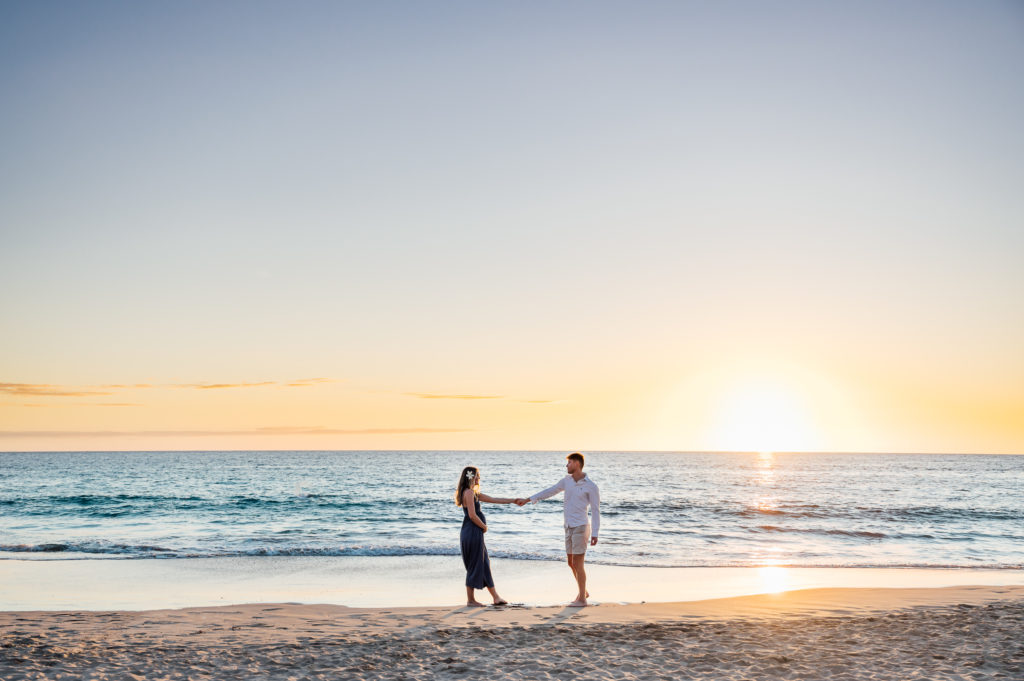 couple holding hands during sunset babymoon by Kona photographer