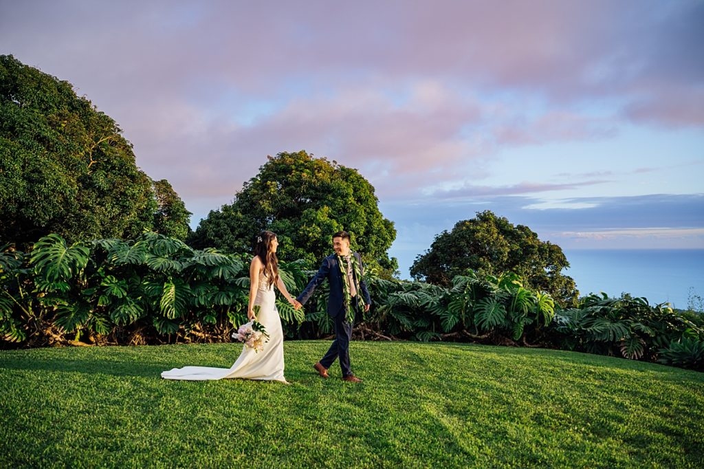 wedding photo of bride and groom walking on the grass while holding hands during their Big Island wedding