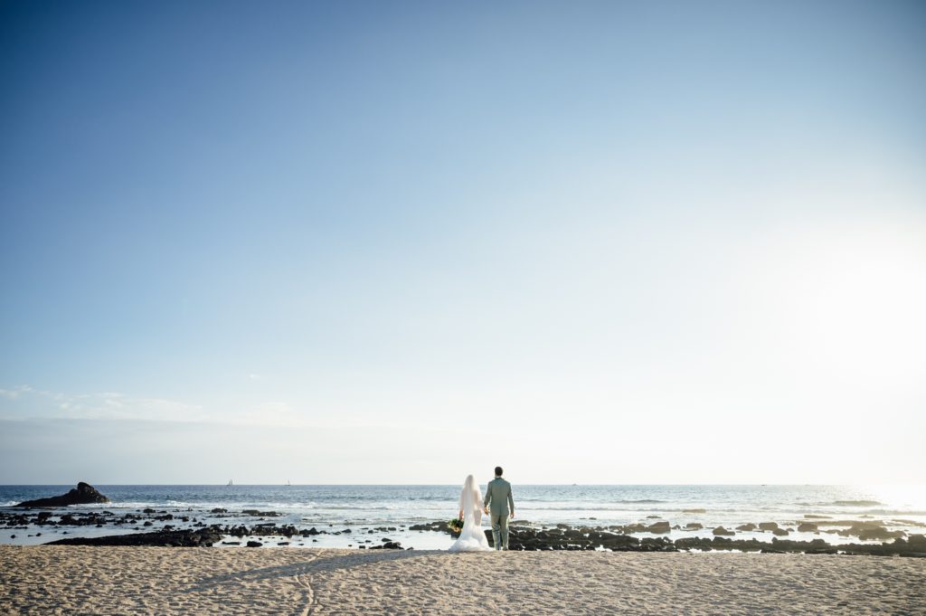 newlyweds holding hands on the beach by Hawaii photographer