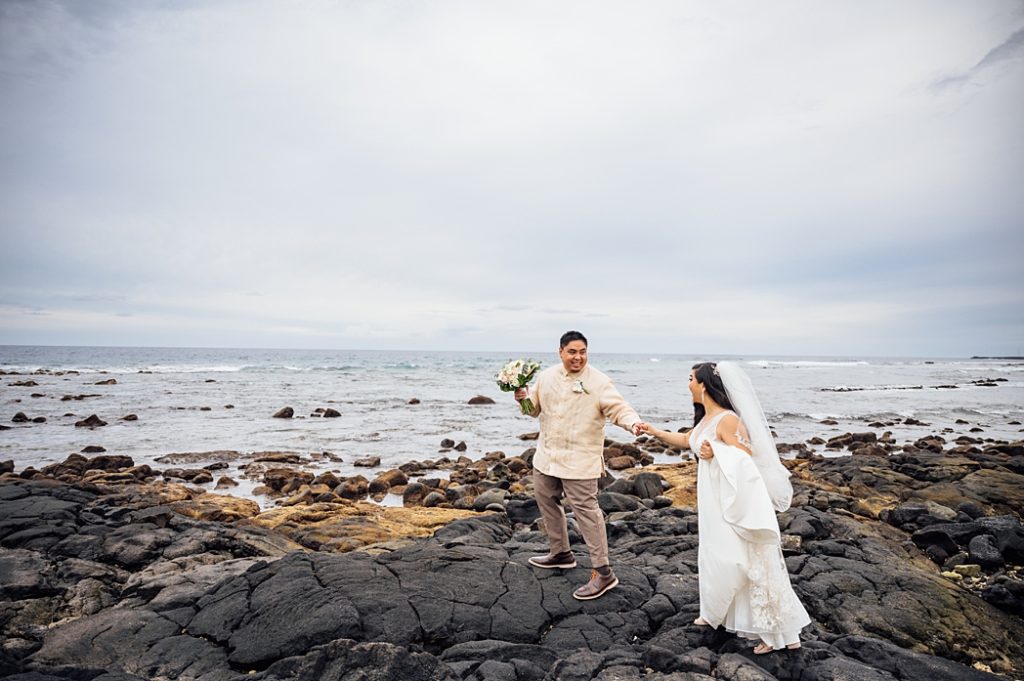 bride and groom holding hands on the lava rocks