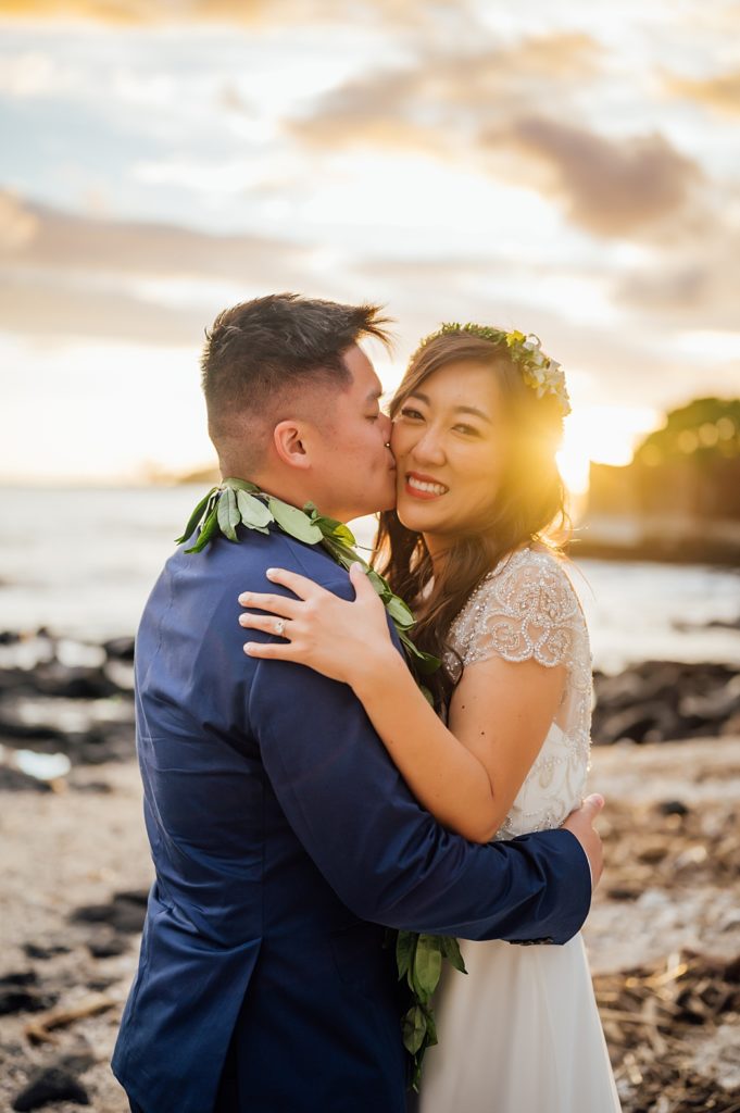 groom kissing the bride's cheeks during sunset at Hawaii beach