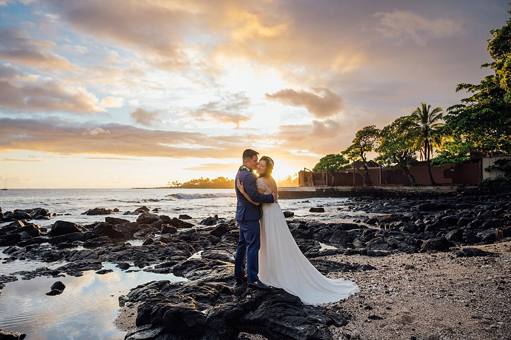 groom kissing bride's cheeks on the lava rocks at Hawaii beach