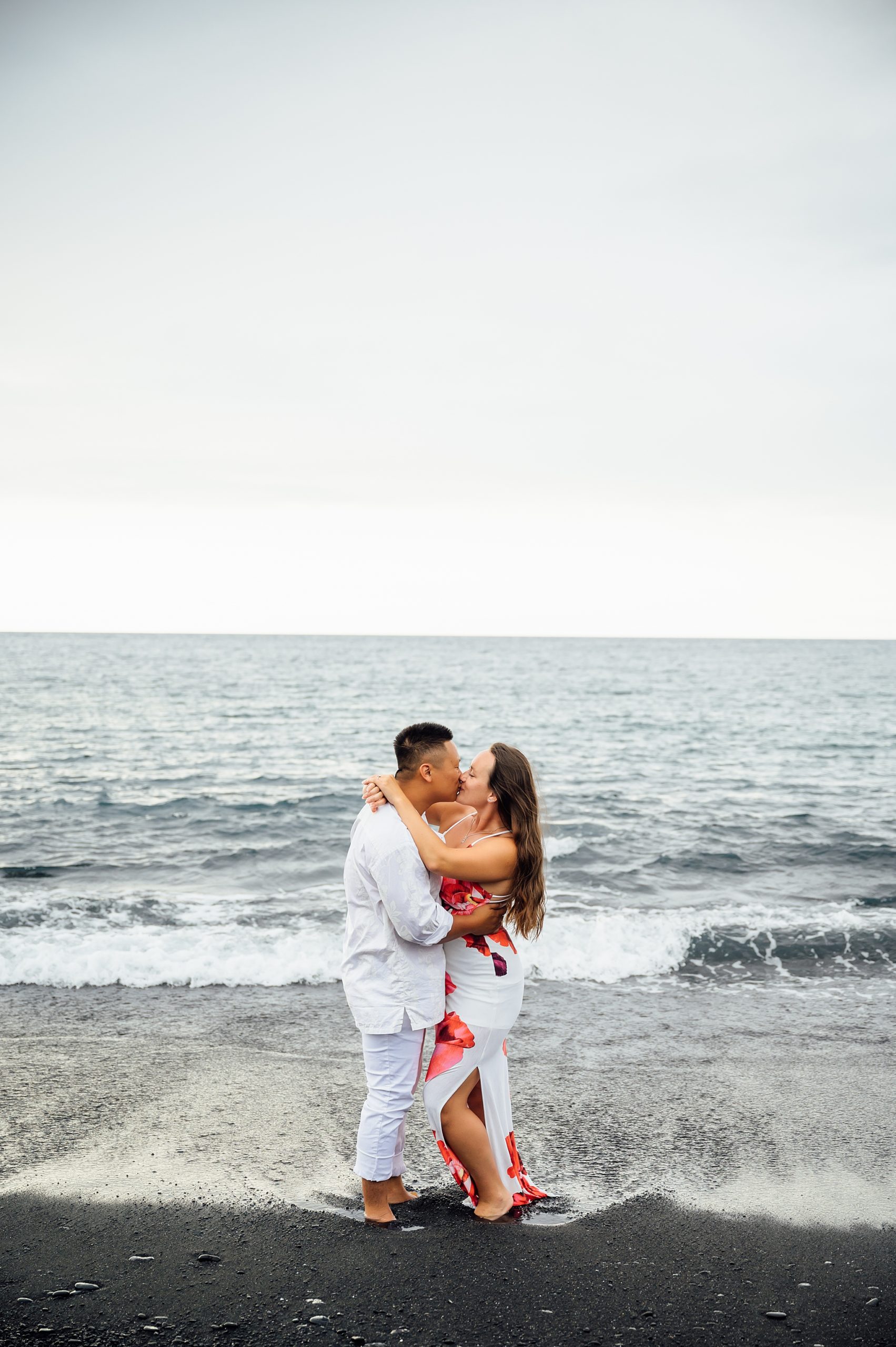 couple kissing at the black sand beach in Hawai