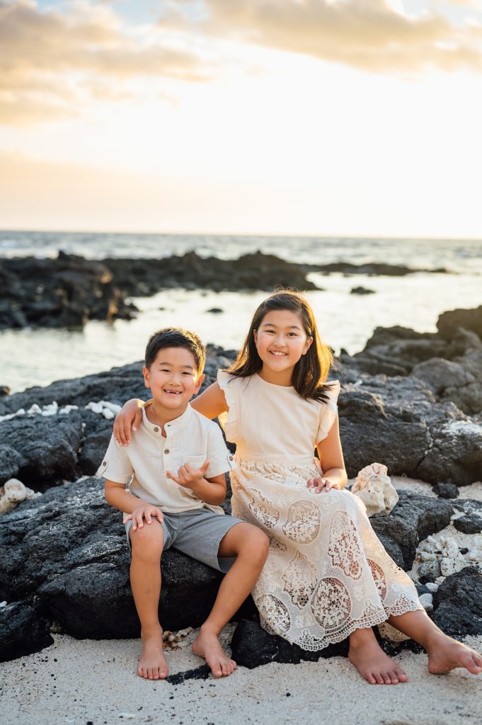 happy siblings sitting on the lava rocks at Hawaii beach