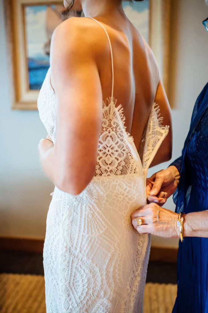 zipping up the dress of the bride by wedding photographer