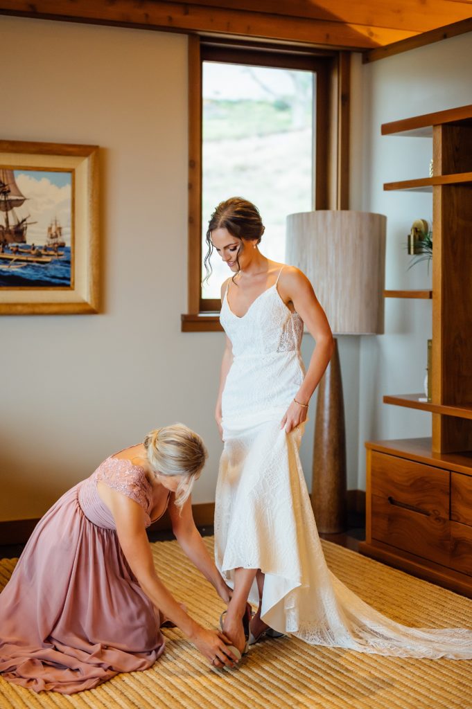 bridesmaid helping bride put on shoes during her Hawaii wedding