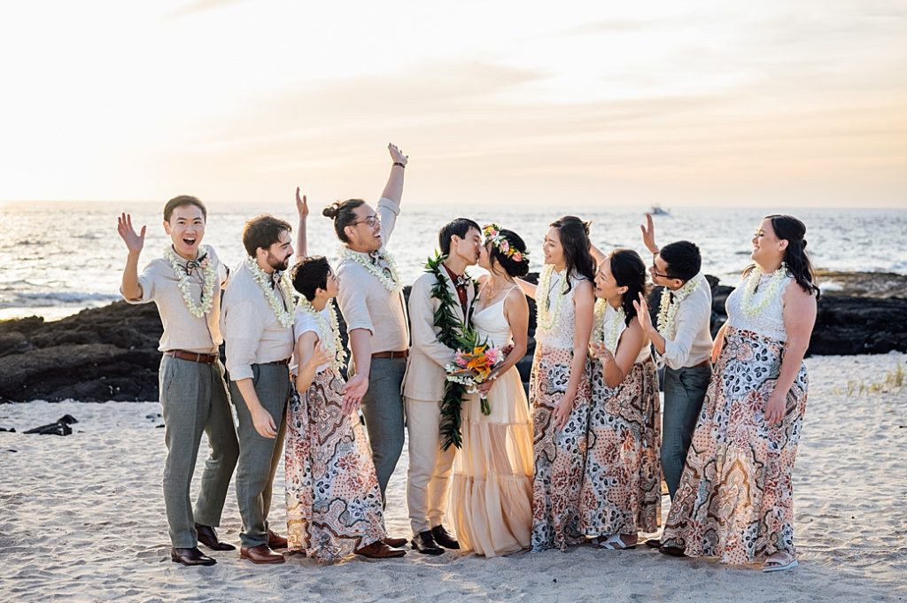 happy wedding party while newlyweds kiss at the beach
