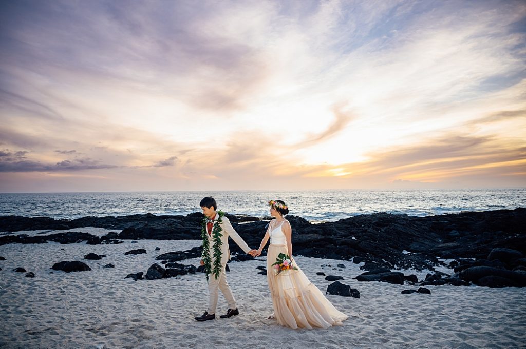 newlyweds holding hands on the white sand by wedding photographer