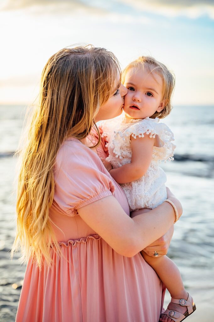 mom kissing daughter's cheeks by Big Island beach photographer